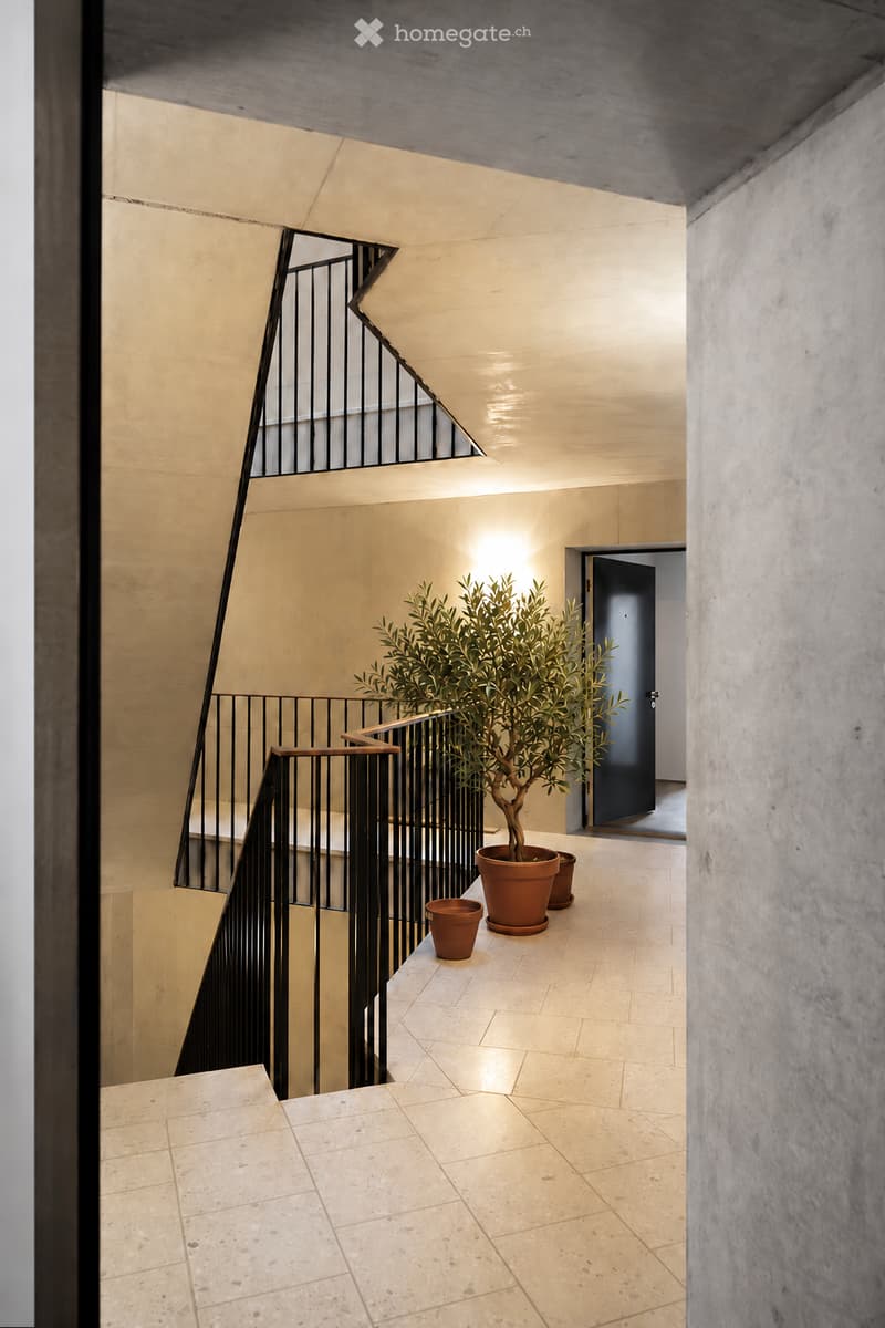 Modern hallway with a staircase, light-colored tiled flooring, and a potted plant on a landing.