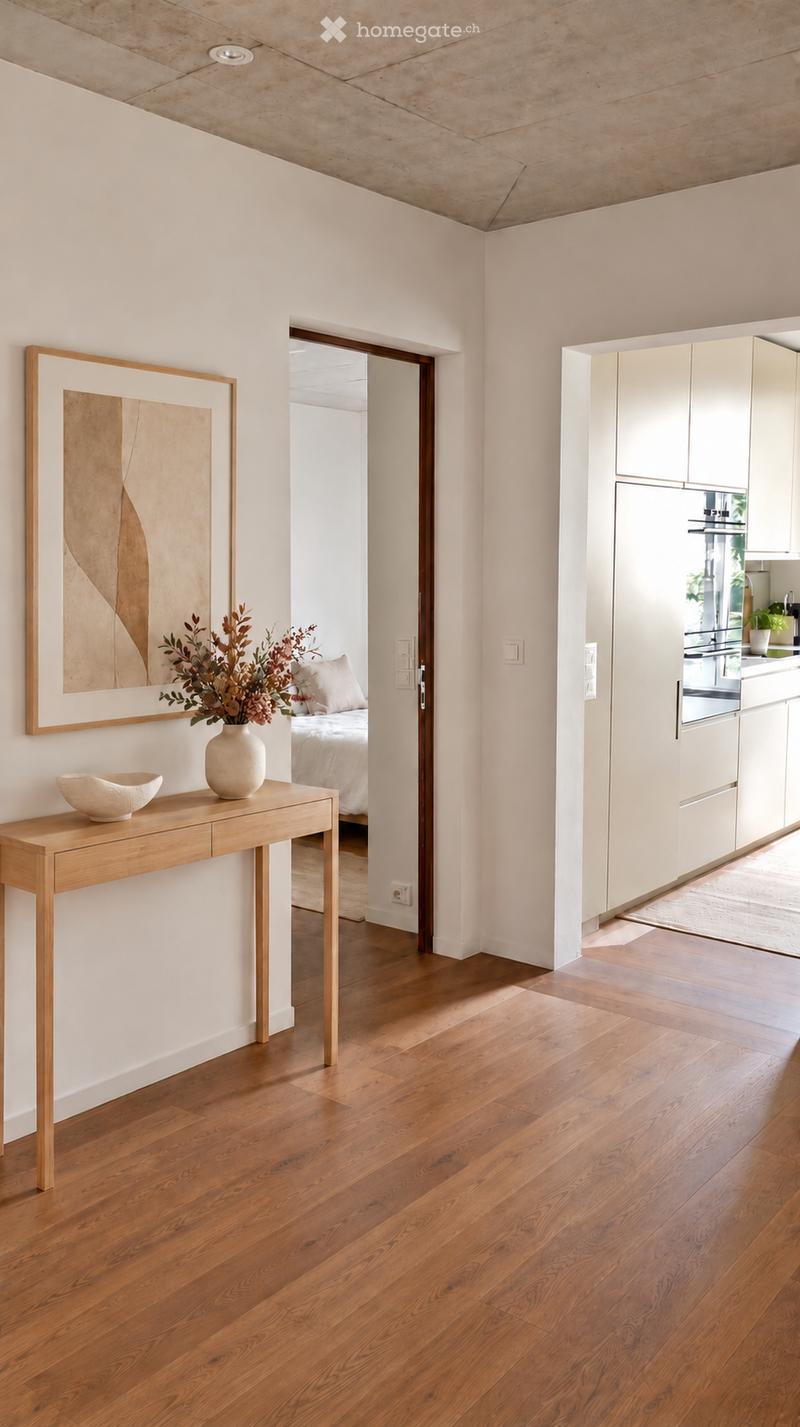 A modern hallway with light wooden flooring, white walls, and a sleek console table with a vase and bowl. The hallway leads to a bedroom and a kitchen area with white cabinets and stainless steel appliances.