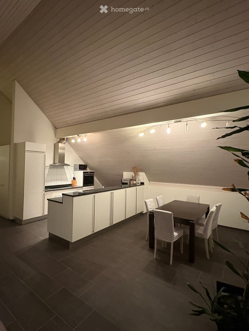 Modern kitchen with white cabinets, dark countertops, and a dining area featuring a table and chairs. The space includes a refrigerator, oven, microwave, and a decorative plant in the corner.