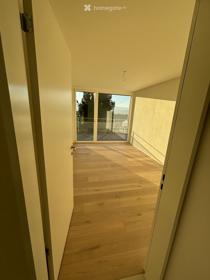 Empty hallway with wooden flooring, white walls, and a sliding glass door leading to an outdoor area.