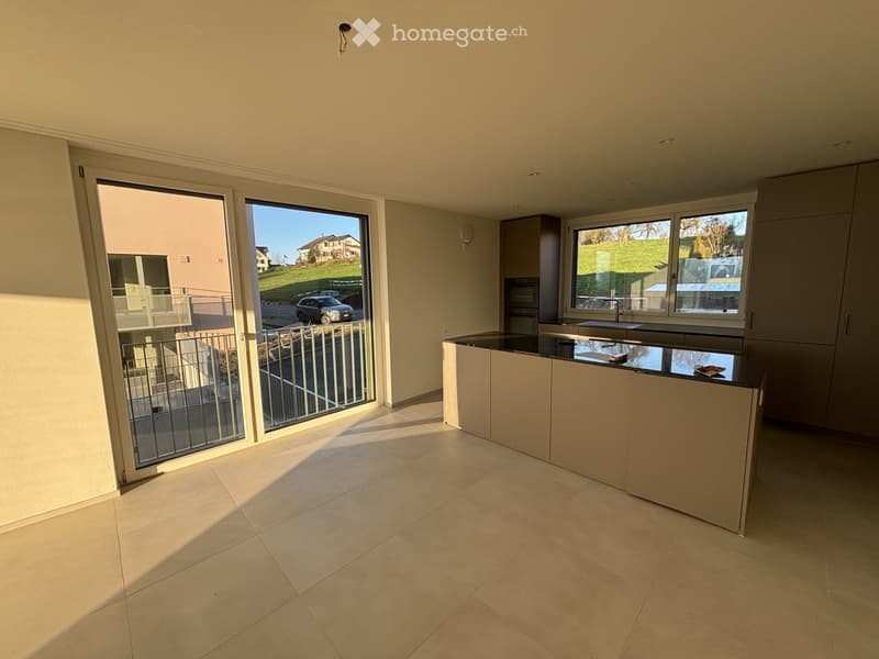 Modern kitchen with light-colored cabinets, a central island, and large windows overlooking a balcony and outdoor area.