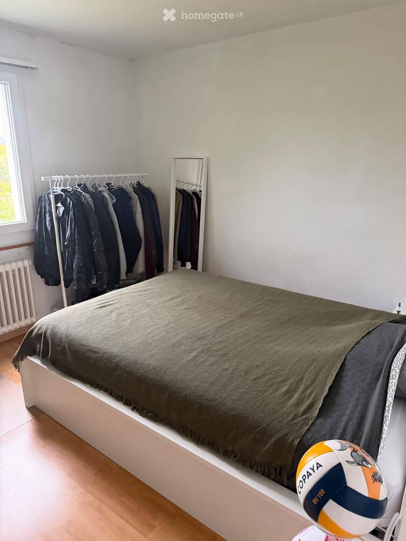 A small bedroom with a single bed, a mirror, a wardrobe, and a volleyball on the floor.