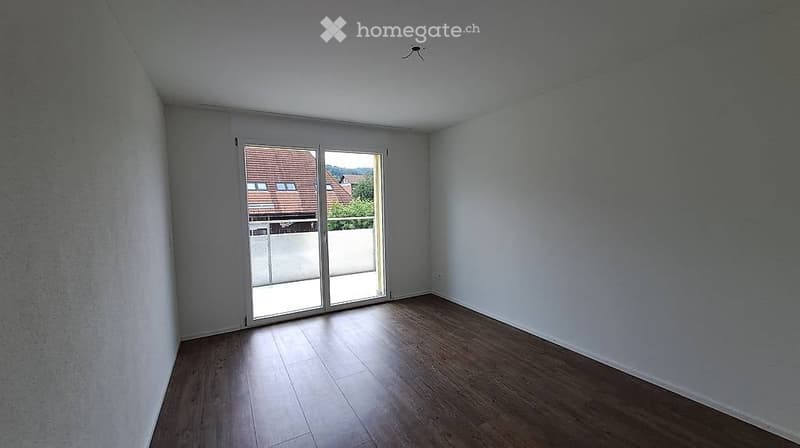 Empty room with wooden flooring, white walls, and large sliding glass doors leading to a balcony.