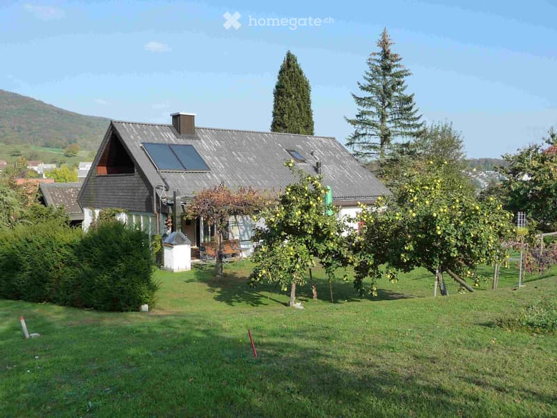 Two-story house with a dark grey roof, solar panels, and a well-maintained garden with fruit trees and a bench.