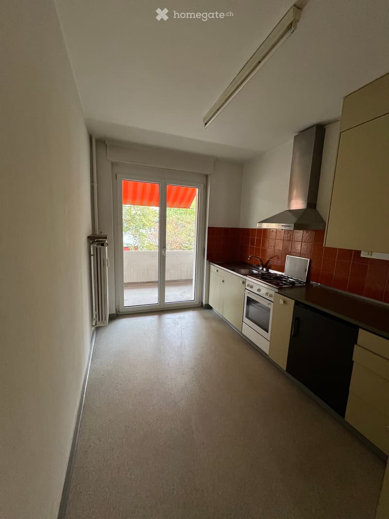 Empty kitchen with white cabinets, a stove, sink, and a sliding glass door leading to a balcony.