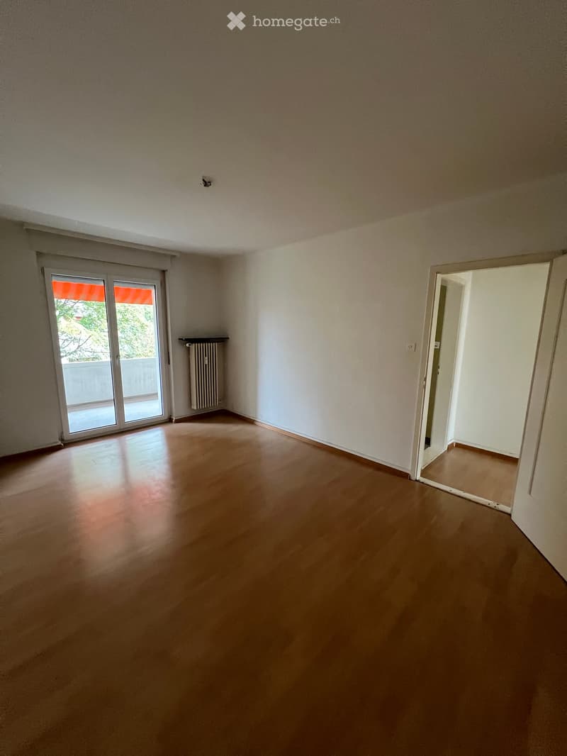 Empty room with wooden flooring, white walls, and a sliding glass door leading to a balcony.
