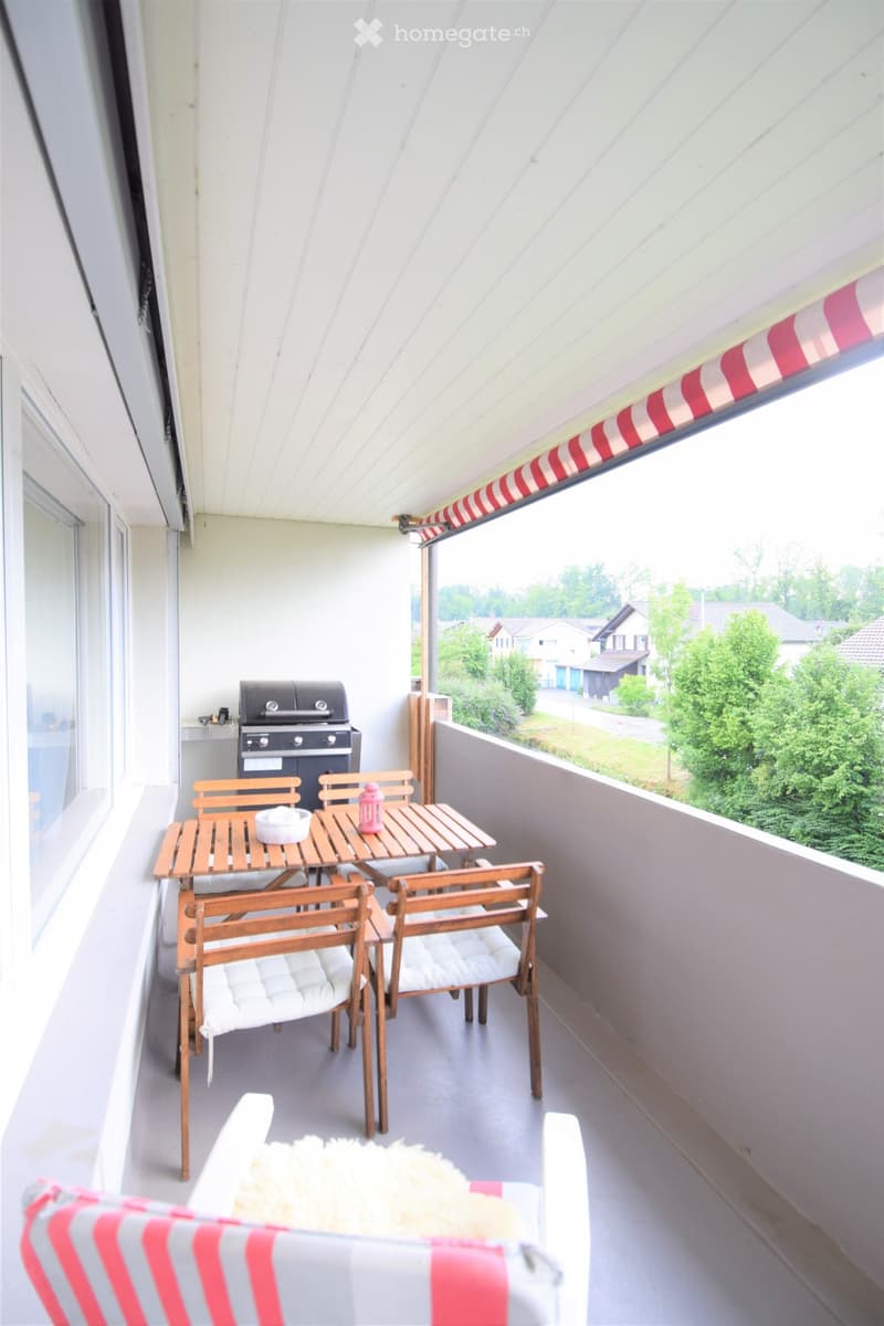 Balcony with a wooden table, four chairs, a grill, and a view of the neighborhood.
