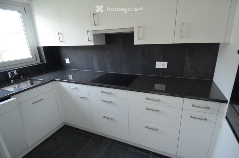 Modern kitchen with white cabinets, black countertops, and a stainless steel sink.