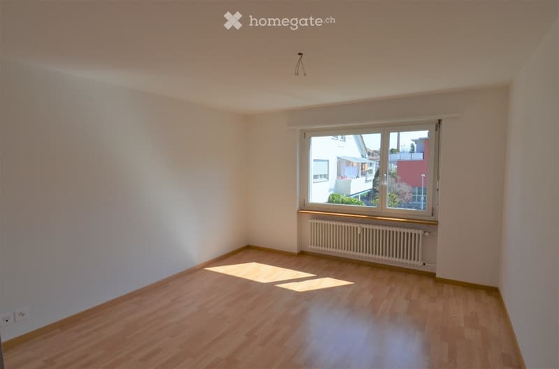 Empty room with wooden flooring, white walls, and a large window with a radiator below it.