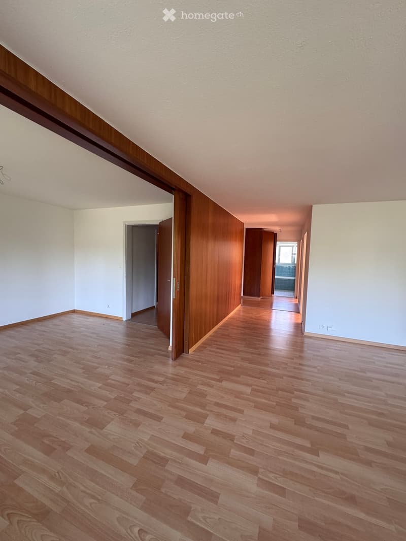 Empty hallway with wooden flooring, white walls, and open doors leading to other rooms.