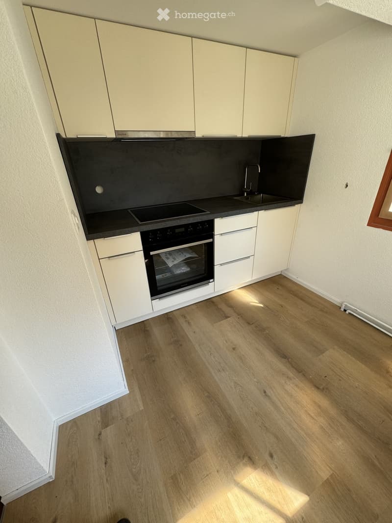 Modern kitchen with light-colored cabinets, black countertops, and a wooden floor. Features an oven, sink, and faucet.