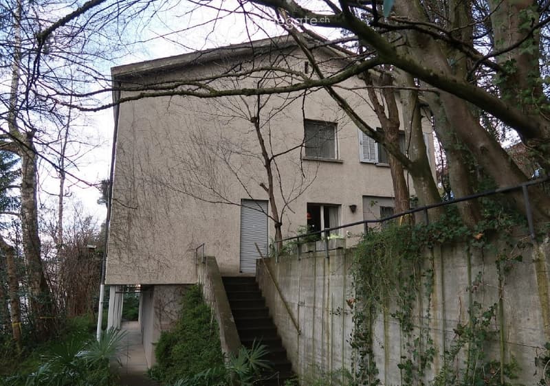 Modern two-story building with a raised ground floor, concrete facade, and steps leading up to the entrance.