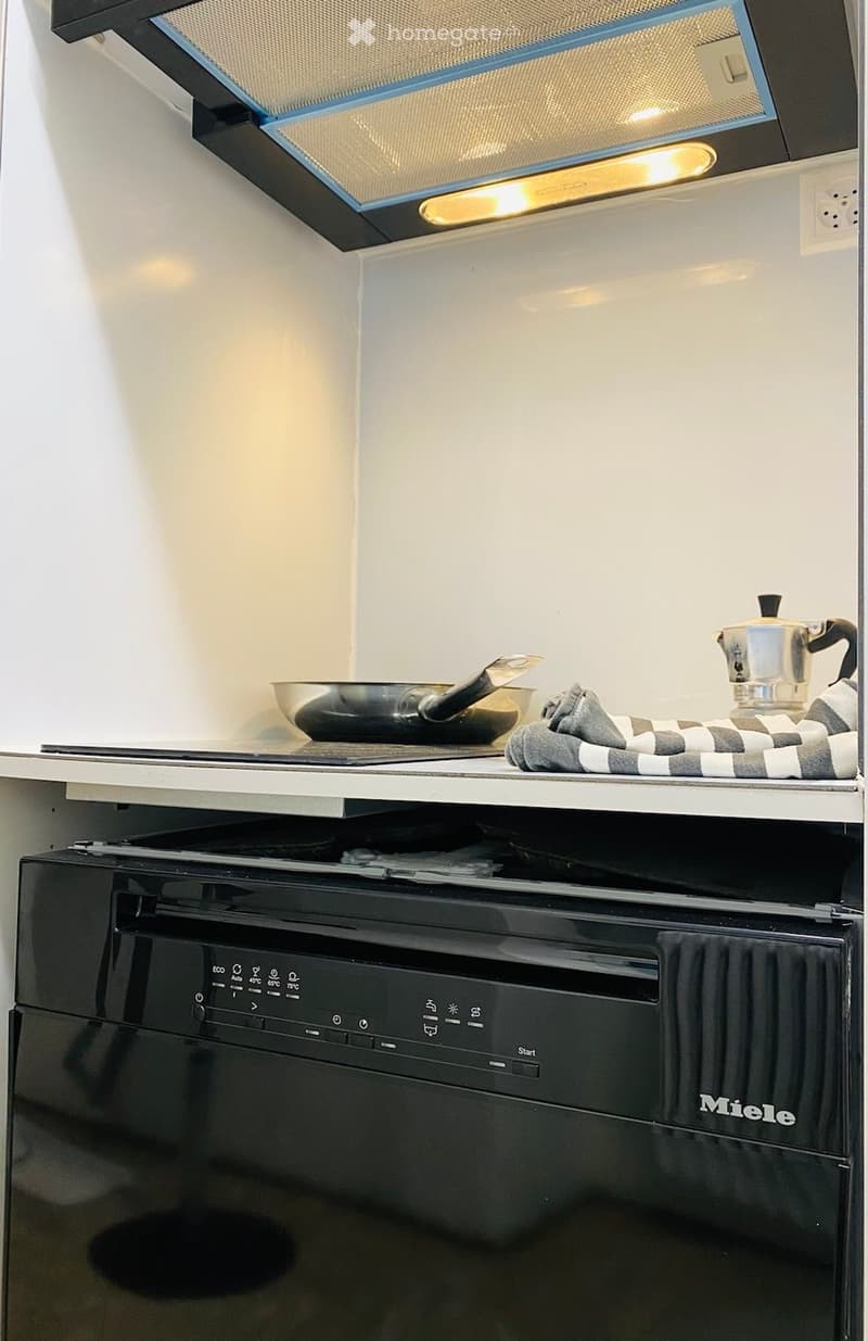Modern kitchen with a built-in oven, a frying pan on the counter, a coffee maker, and a checkered cloth.