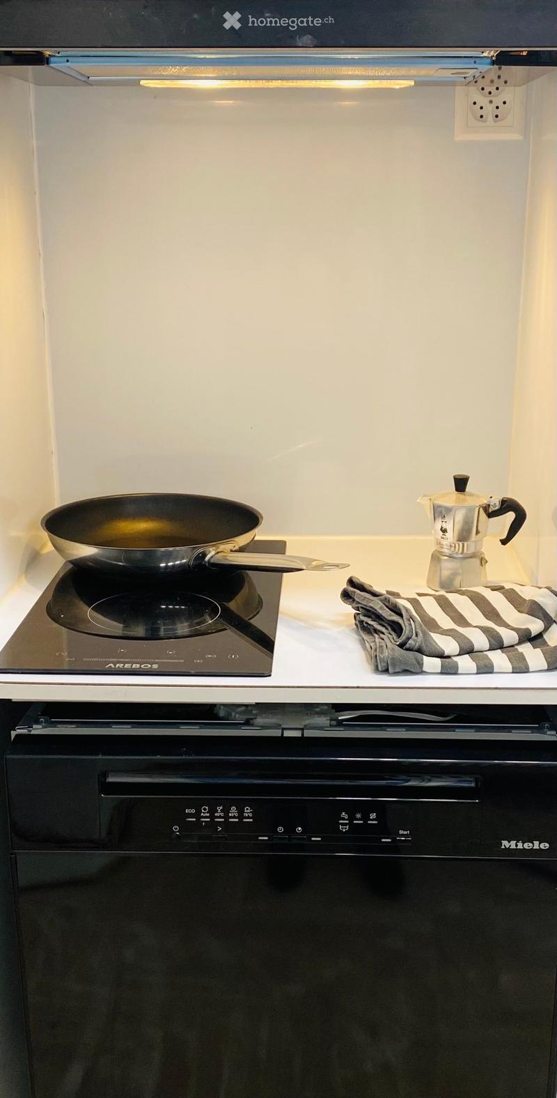 Modern kitchen with an induction stove, a dishwasher, a frying pan, a coffee maker, and a striped cloth on the counter.