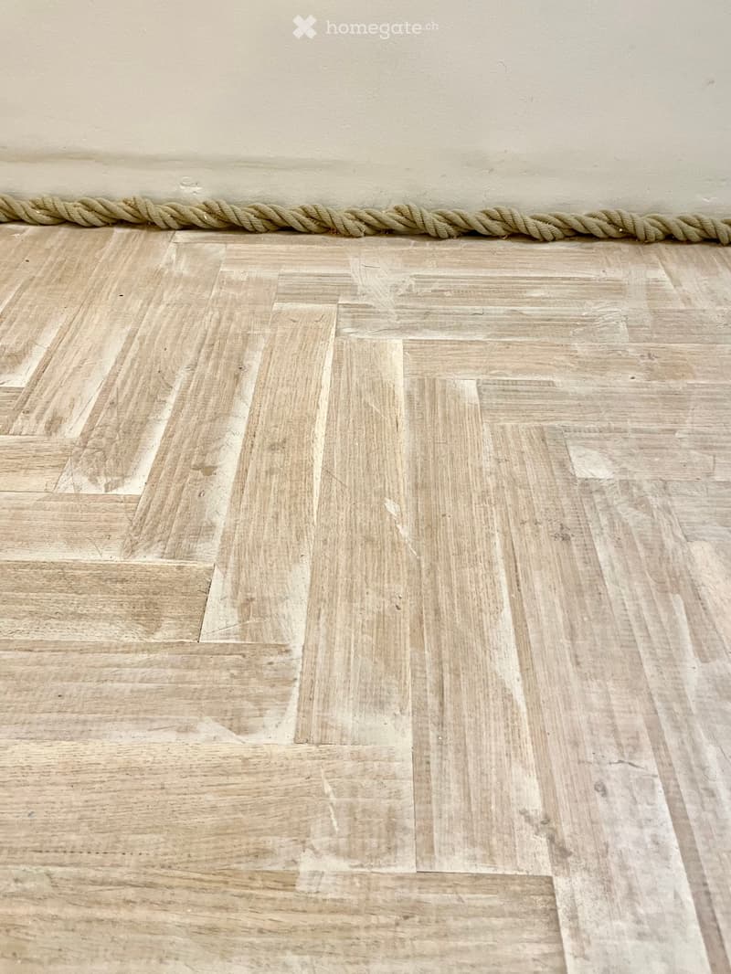 Empty room with light wooden parquet flooring and a rope along the top edge of the wall.