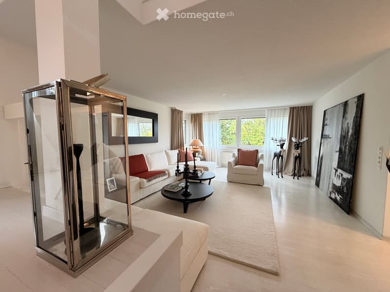 Modern living room with white walls, large windows, a white sofa with red cushions, a black coffee table, an armchair, a table lamp, and decorative items including a large mirror and artwork.