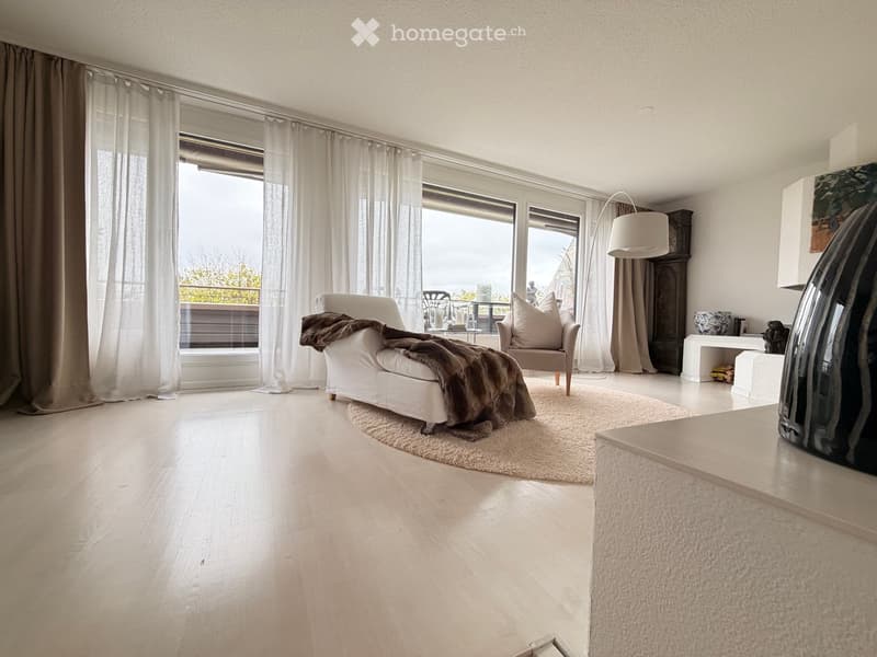 Modern living room with large windows and balcony access, featuring a white sofa, armchair, coffee table, floor lamp, and decorative vase.