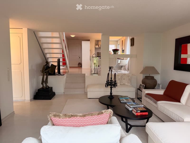 Modern living room with white walls, light wood flooring, and contemporary furniture including a white sofa, ottoman, coffee table, and decorative items.