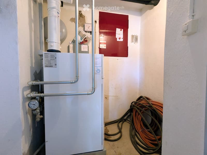Utility room with a white boiler, metal pipes, and a coiled orange cable reel on the floor.