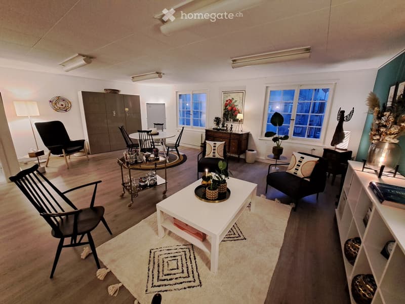 Modern living room with a white coffee table, black sofa, dining area with chairs and table, and decorative items including plants and lamps.