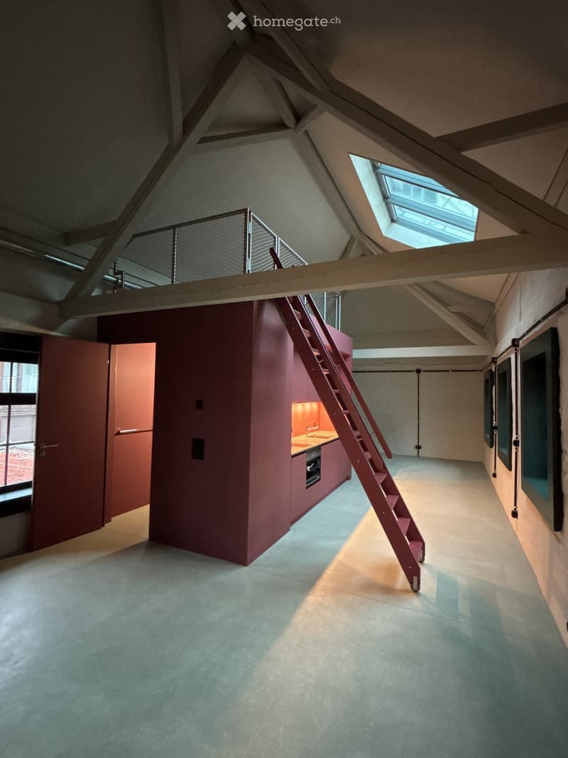 Loft-style room with exposed wooden beams, a staircase leading to an upper level, a compact kitchen area, and large windows allowing natural light.