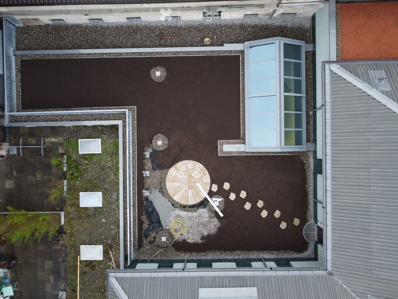 Roof terrace with a circular patio, gravel, and surrounding buildings.
