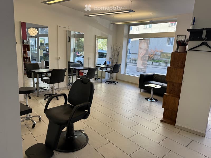 Modern salon with tiled floor, large windows, multiple chairs, a sofa, and mirrors.