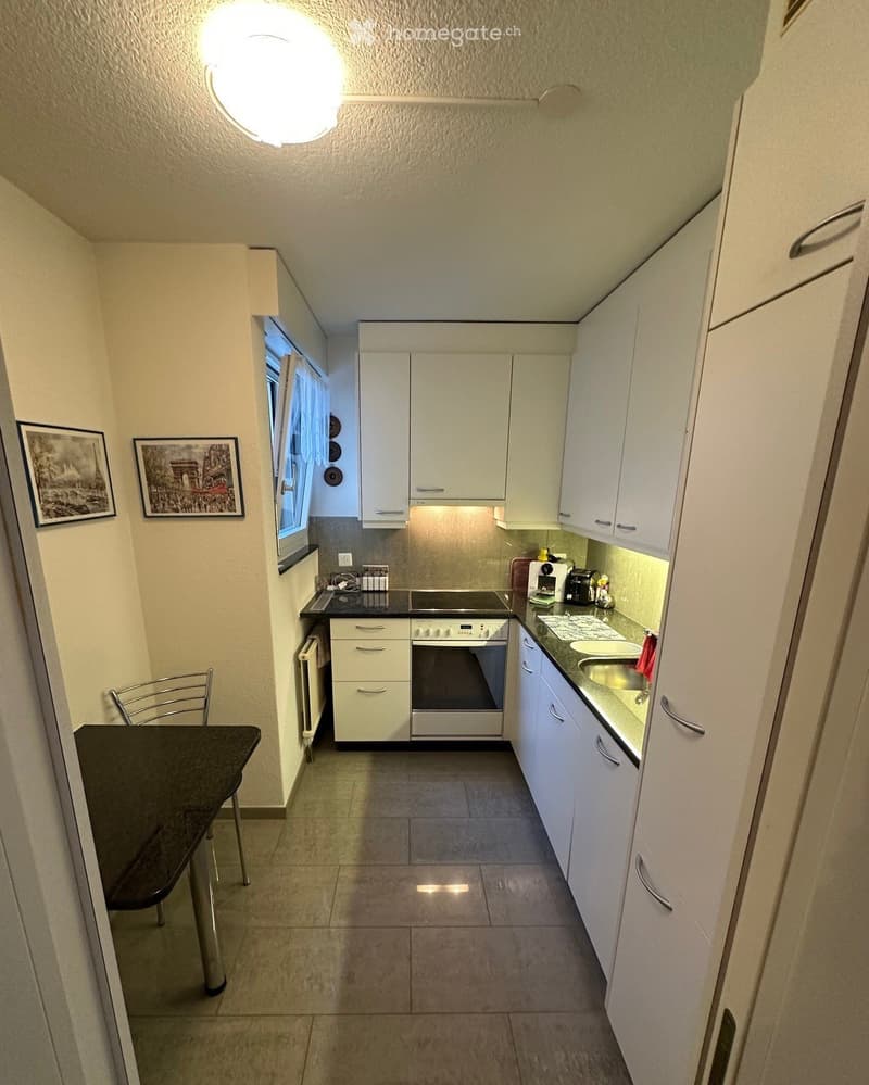 Modern kitchen with white cabinets, stainless steel appliances, a black countertop, and a small dining area with a table and chair.