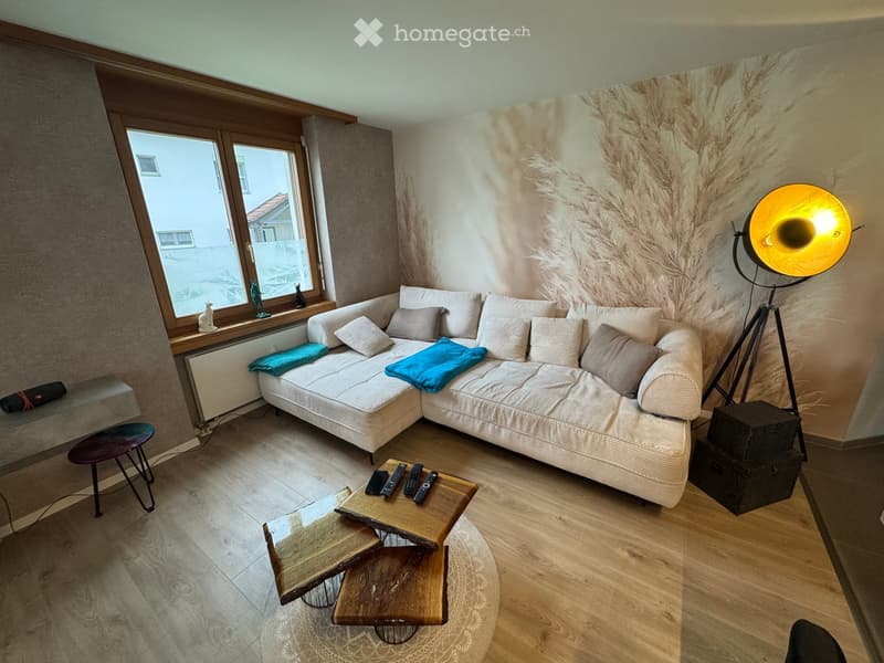 Modern living room with a white sectional sofa, wooden coffee table, floor lamp, and decorative items on the windowsill.