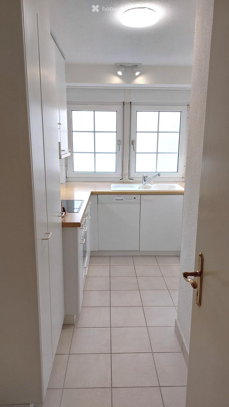 Modern kitchen with white cabinets, tiled floor, and a double sink under windows.