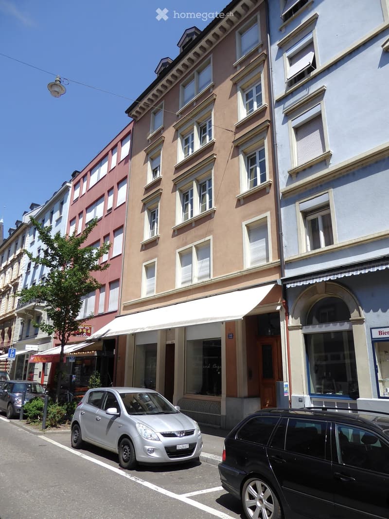 Multi-story building with awnings, storefronts, and parked cars in front.