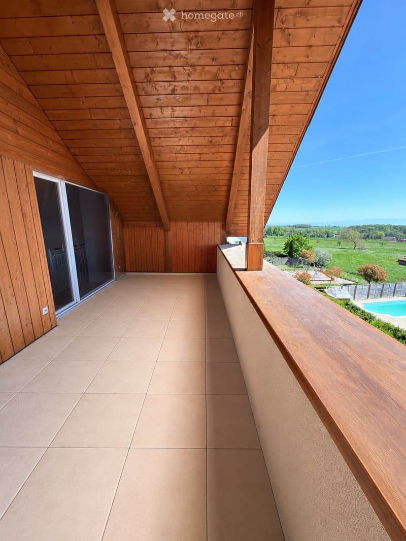 Wooden balcony with tiled floor, wooden railing, and open view of a green landscape and swimming pool.