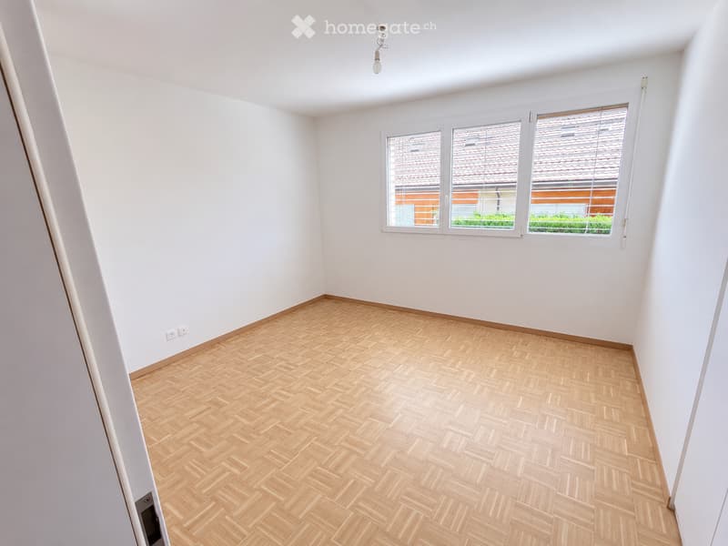 Empty room with light wooden herringbone flooring, white walls, and large windows with blinds. No furniture or equipment present.