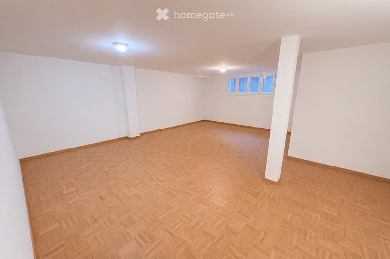 Empty room with wooden herringbone flooring, white walls, and three windows on one side. The room has a simple, clean design with no furniture or decorations.