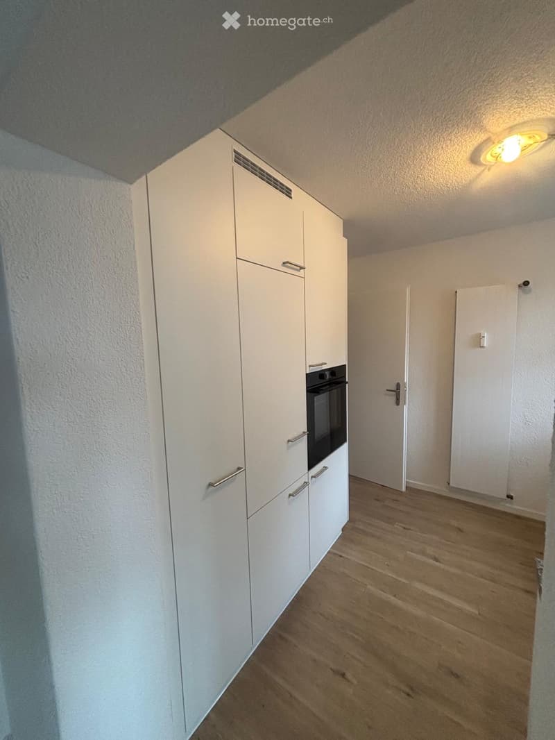 Empty room with white cabinets, wooden flooring, and a built-in oven. No furniture or personal items present.