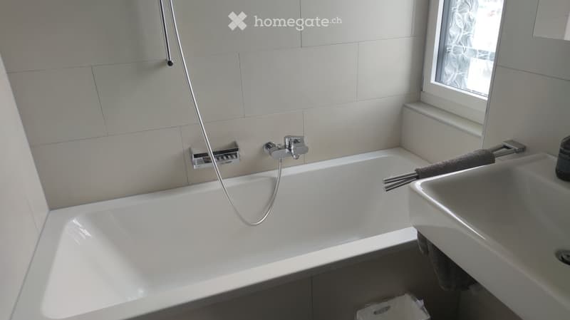 Modern bathroom with a white bathtub, a sink, a towel, and a window with a curtain.