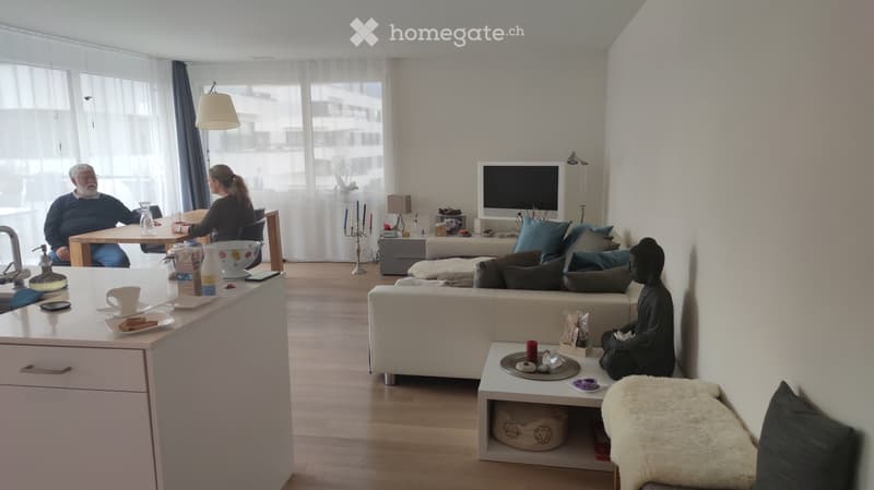 Bright living room with a white sofa, coffee table, dining table, chairs, television, and decorative items including a statue and candles.