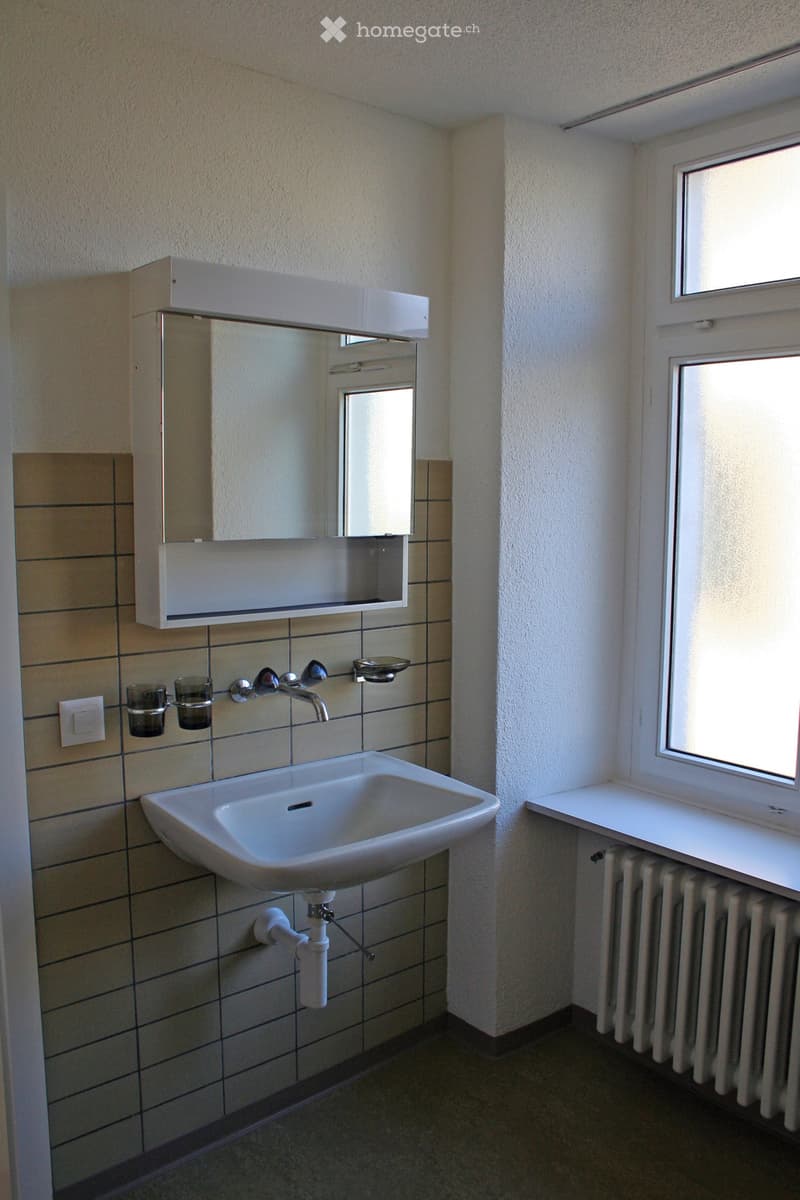 Bathroom with a white sink, faucet, mirror cabinet, two cups, and a radiator under a window.