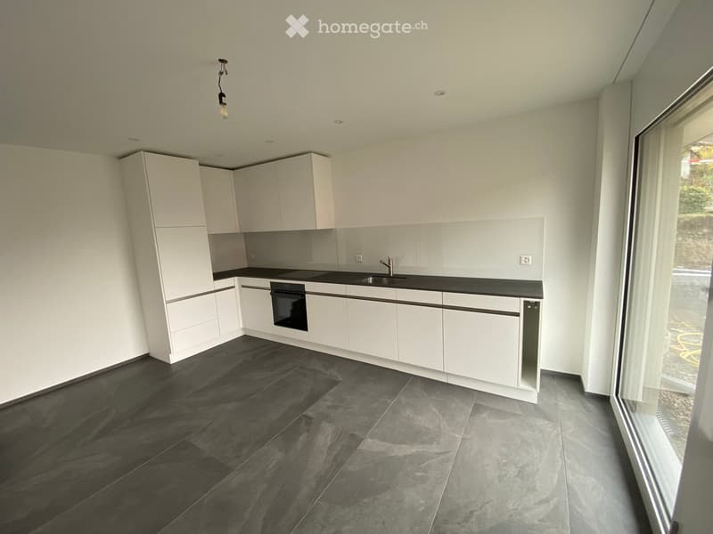Modern kitchen with white cabinets, dark countertops, and a black tiled floor. Features a sink, oven, and ample storage space.