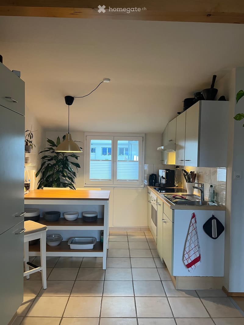 Modern kitchen with white cabinets, a central island, and a sink area. Includes a stool, coffee maker, oven, and various kitchen utensils.