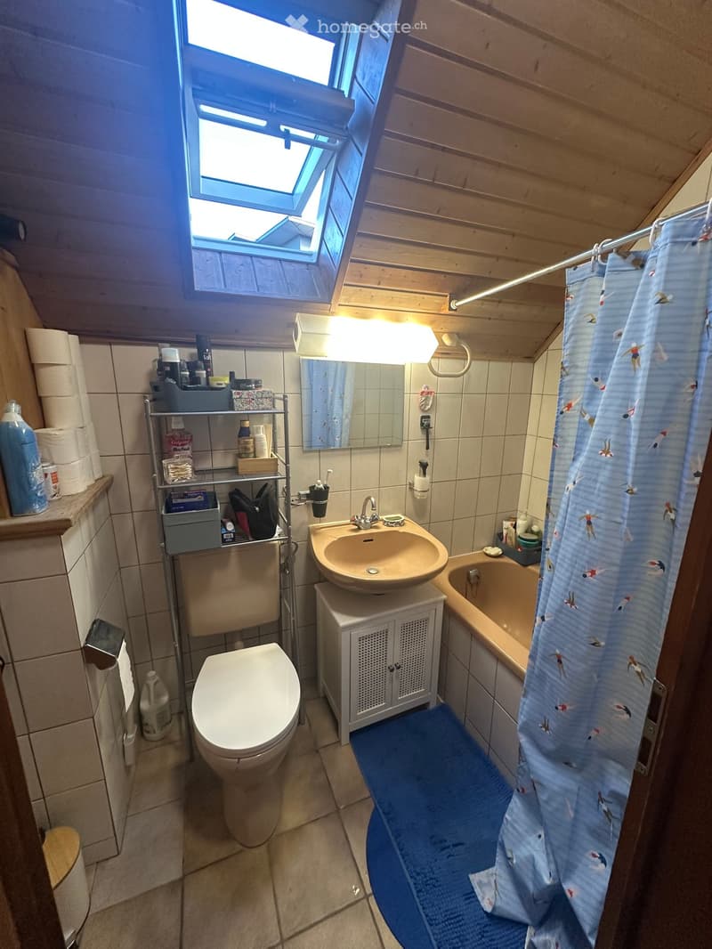 Bathroom with a toilet, sink, bathtub, mirror, and shower curtain. Features a wooden ceiling and tiled walls.