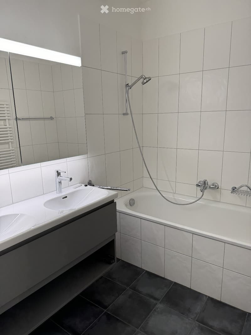 Modern bathroom with white tiles, a double sink, a bathtub, a mirror, and a radiator.