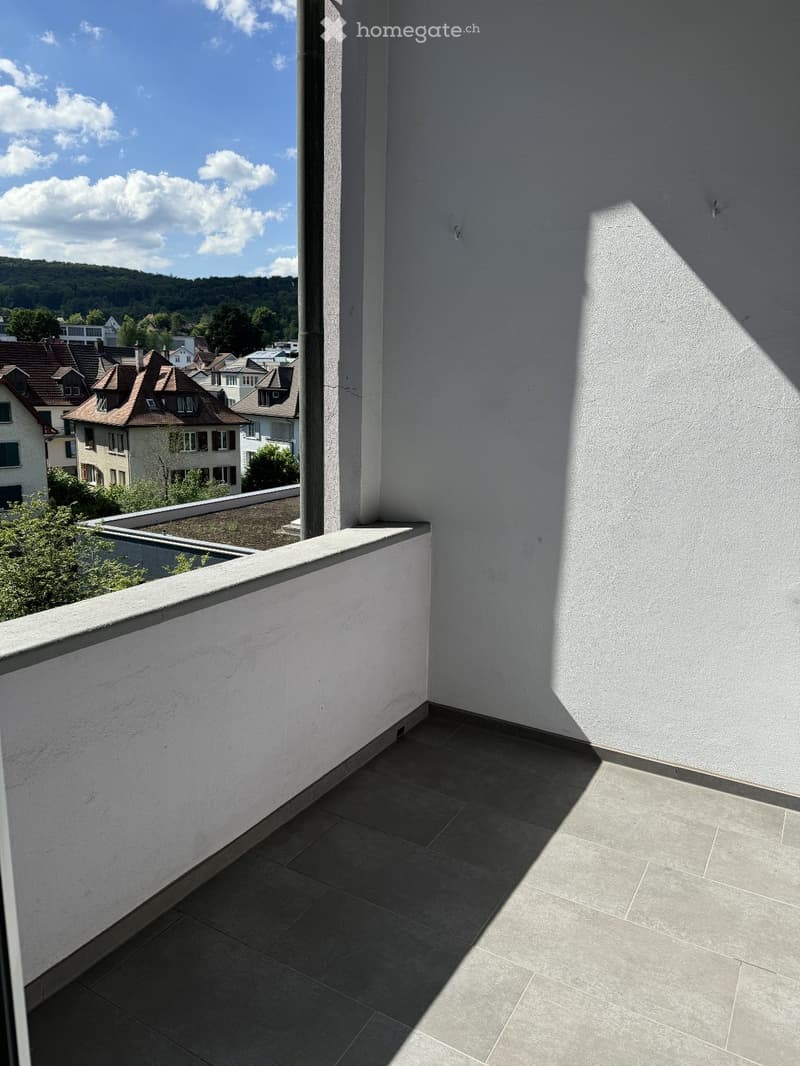 Balcony with tiled floor, white walls, and a view of a town with houses and greenery.