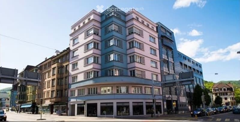 Multi-story building with a mix of pink and blue facades, large windows, and a modern architectural style.
