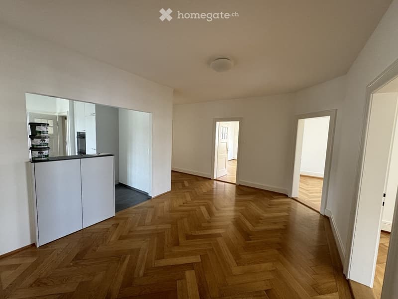 Empty hallway with wooden herringbone flooring, white walls, and several doorways leading to other rooms.