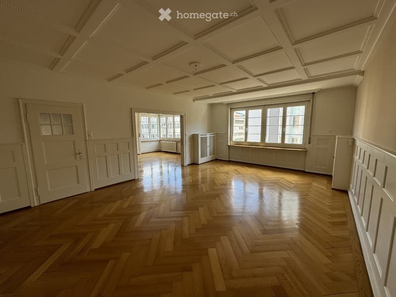Empty room with wooden herringbone flooring, white walls, large windows, and decorative ceiling moldings.