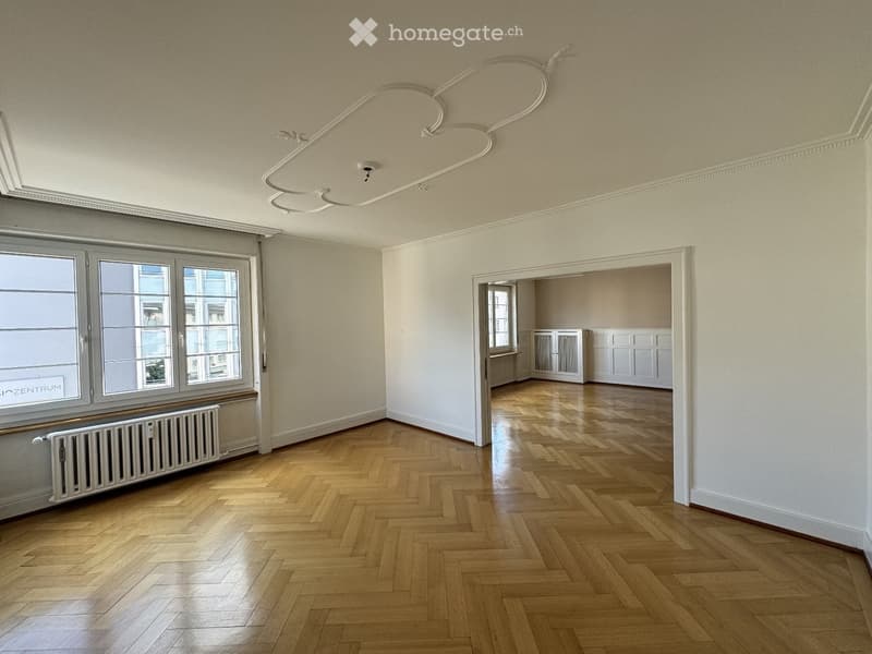 Empty room with wooden herringbone flooring, large windows, and white walls. No furniture or equipment present.