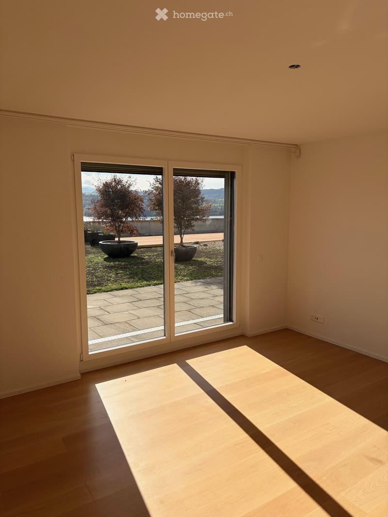 Empty room with wooden flooring and large sliding glass doors leading to a patio with potted plants.