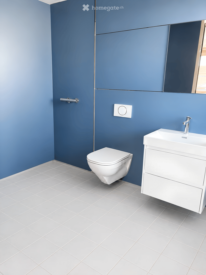 Modern bathroom with blue walls, white tiled floor, toilet, sink with faucet, and mirror above the sink.