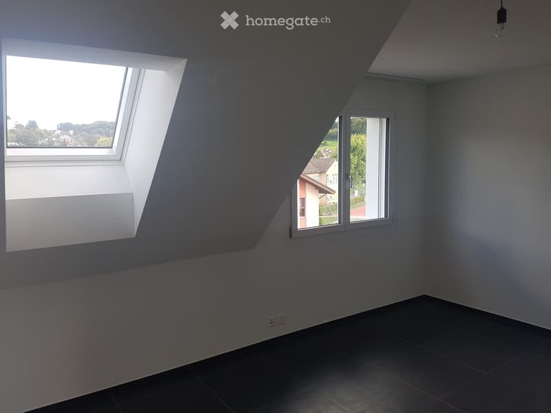 Empty room with slanted ceiling, large windows, and dark tiled floor. No furniture or equipment present.